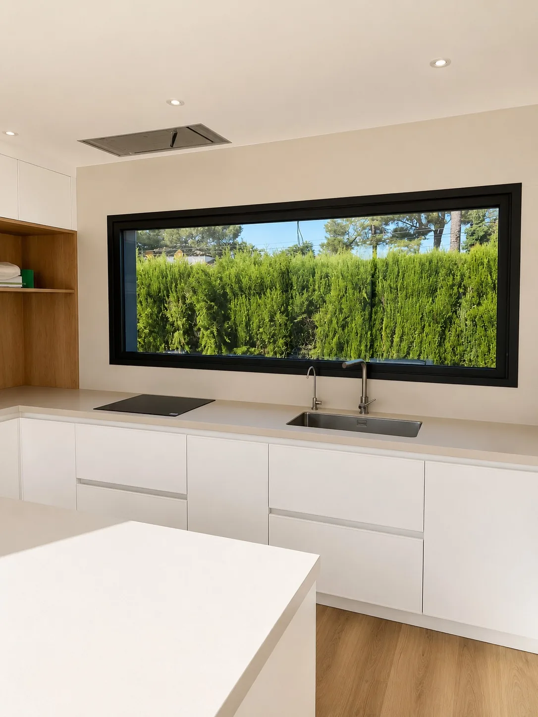 Cocina con fregadero bajo una ventana panorámica que enmarca el seto verde